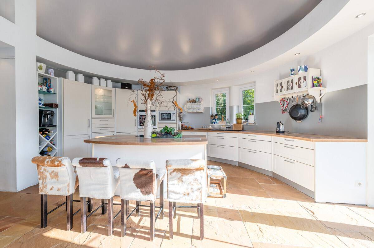 Moderne, offene Küche mit weißer Einbauküche, Kücheninsel und Steinboden in geschwungener Architektur.