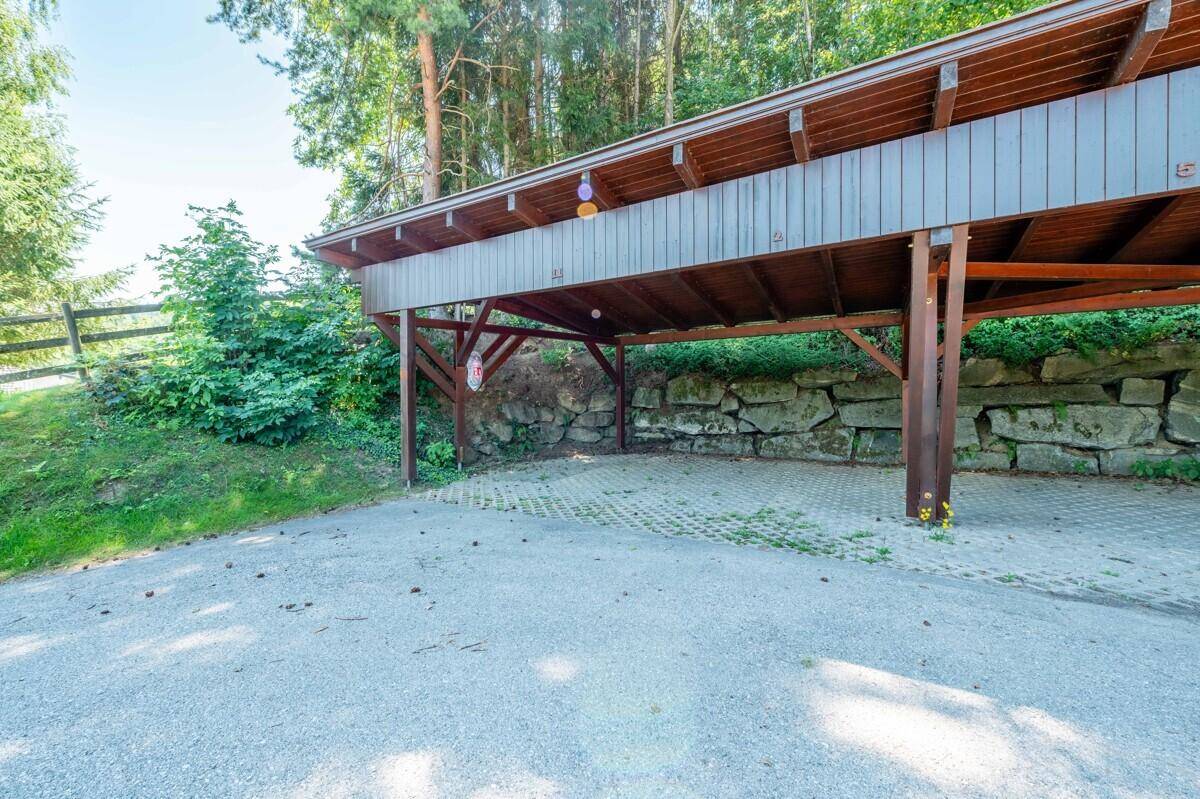 Geräumiger Holzcarport mit gepflastertem Boden, umgeben von Natur.