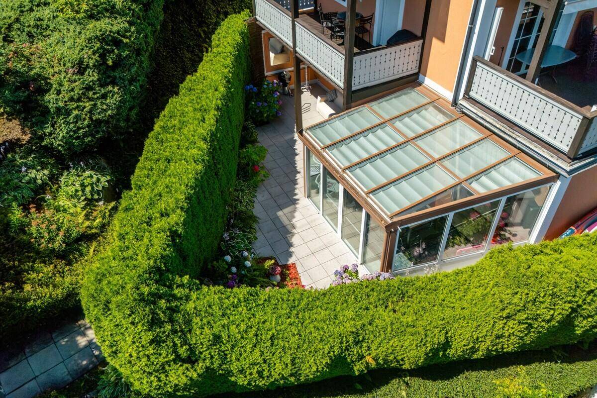 Blick von oben auf den Wintergarten und die Terrasse, geschützt durch eine Hecke.