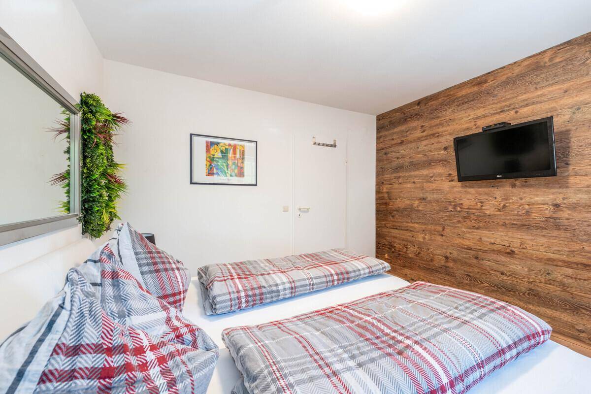Schlafzimmer mit Holzwand, Doppelbett und Flachbildfernseher, bereit für erholsame Nächte.
