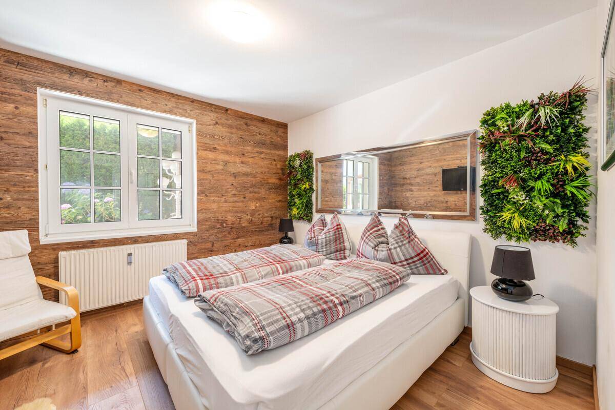 Gemütliches Schlafzimmer mit Holzwand, Doppelbett und dekorativen Pflanzenpaneelen an der Wand.