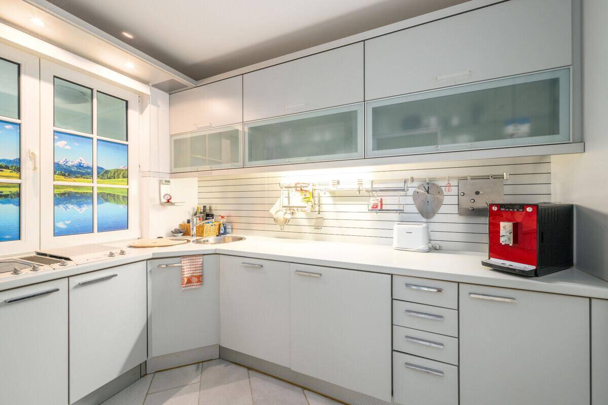 Moderne Küche mit weißen Schränken, integrierten Geräten und einem Fenster mit Bergpanorama.