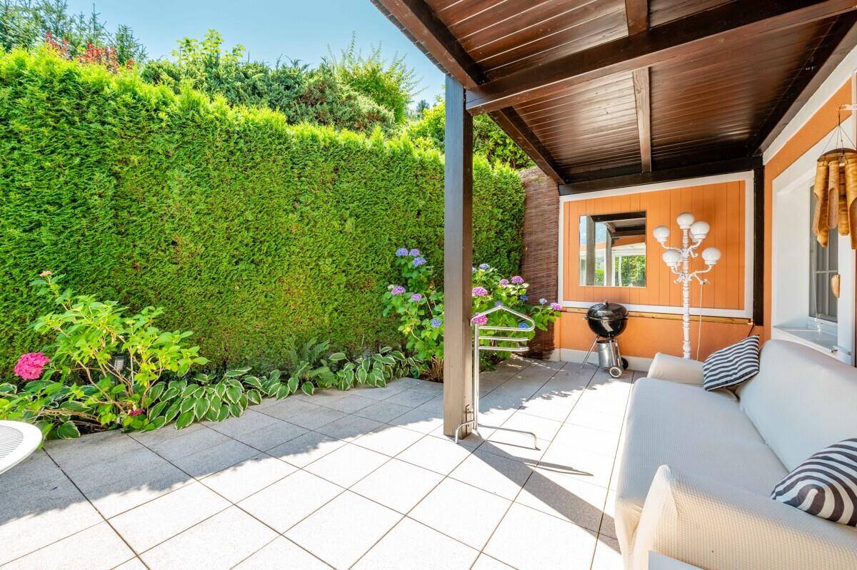 Gemütliche überdachte Terrasse mit Sofa, Grill und hoher Hecke für Privatsphäre.