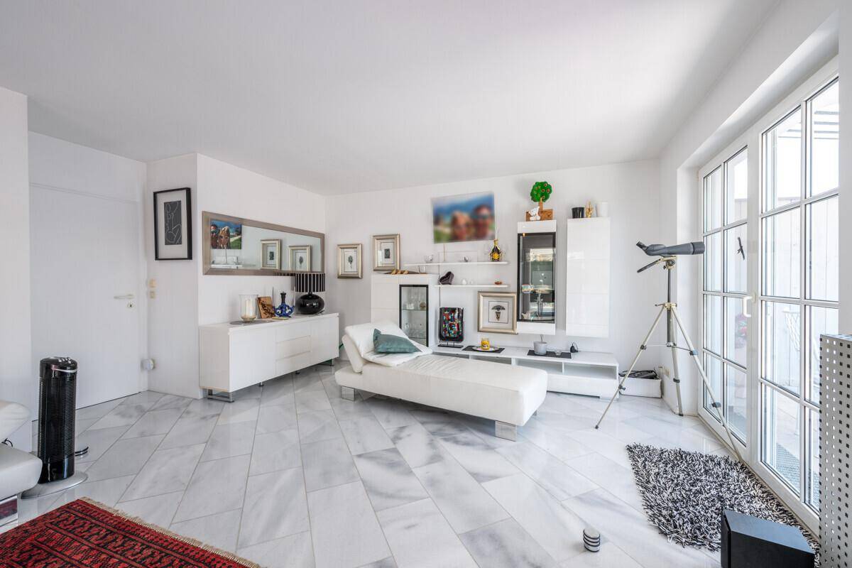 Helles Wohnzimmer mit Marmorboden, weißer Chaiselongue und großen Fenstern zum Garten.