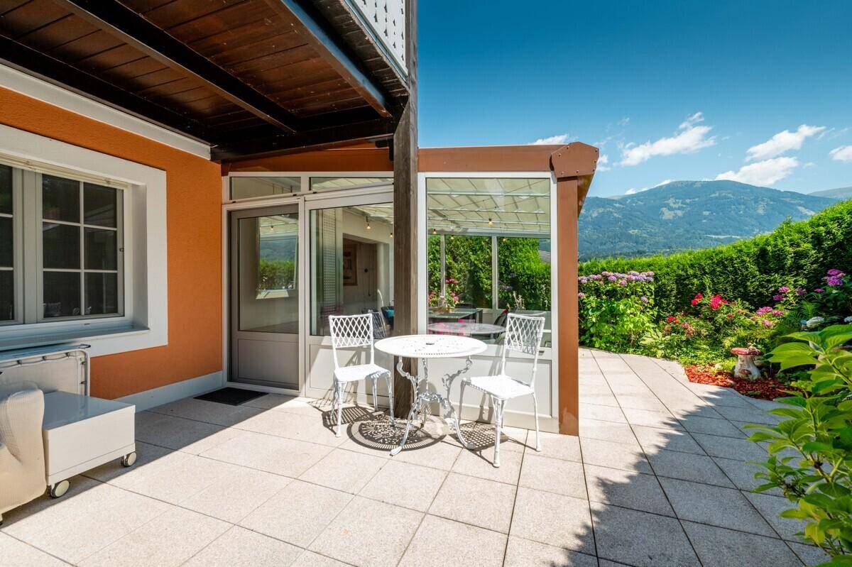 Helle Terrasse mit Sitzgelegenheiten und Blick auf die Berge und den Garten.