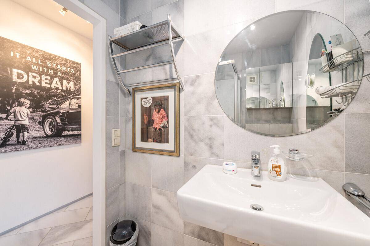 Badezimmer mit Marmorfliesen, Waschbecken und einem runden Spiegel, der den Raum erweitert.