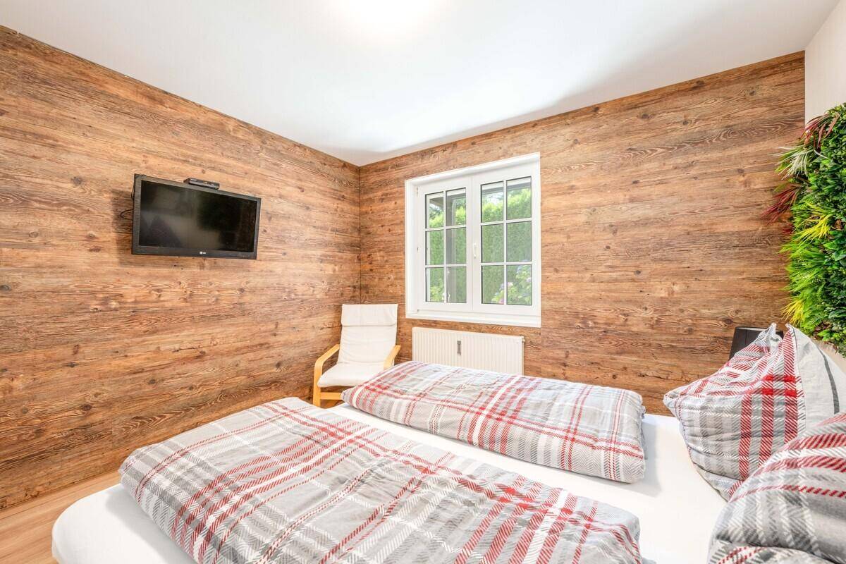 Schlafzimmer mit Holzwand, Doppelbett und Flachbildfernseher, hell durch großes Fenster.