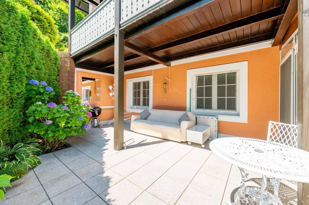 Überdachte Terrasse mit Sitzgelegenheiten, Grill und Blick auf den grünen Garten.