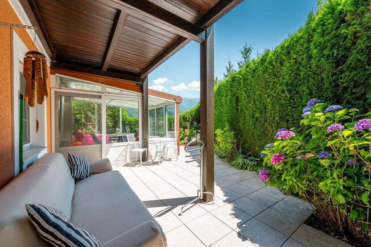 Überdachte Terrasse mit Sofa und Blick auf den Garten sowie den angrenzenden Wintergarten.