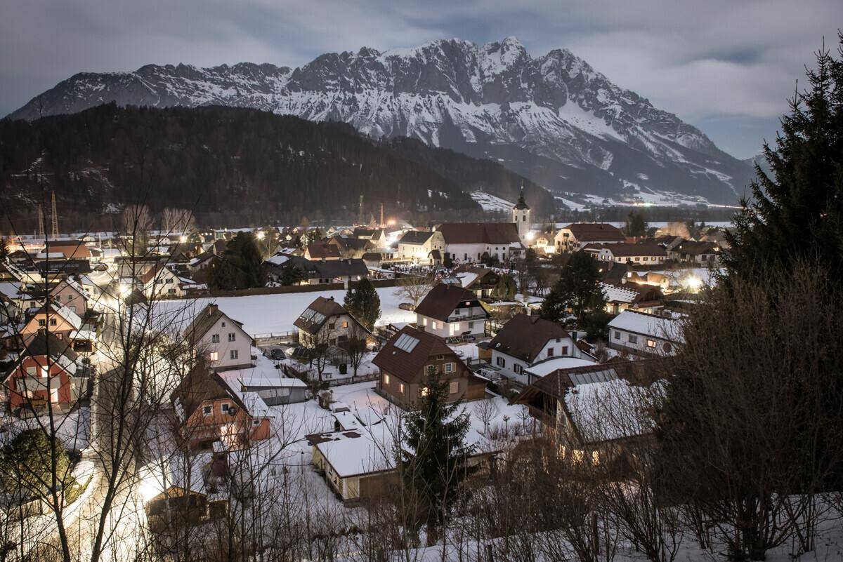 Winterliche Abendstimmung über einem verschneiten Dorf mit beleuchteten Häusern.