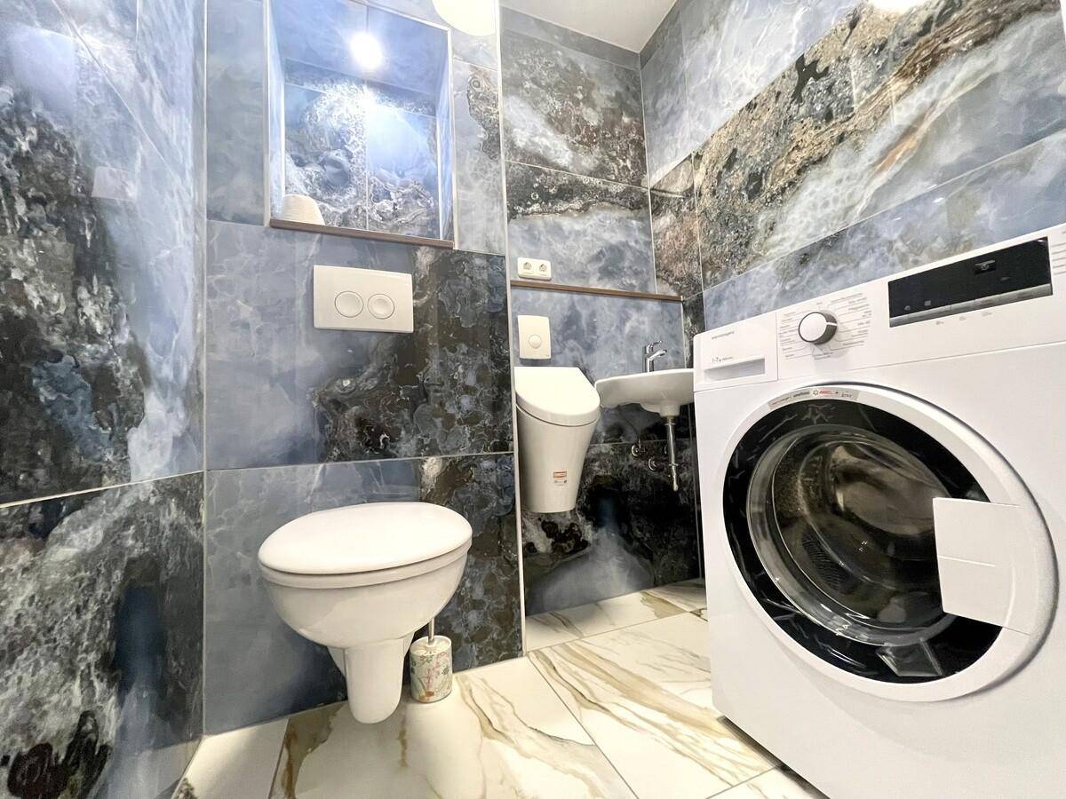 Praktisches Badezimmer mit WC, Waschbecken und Waschmaschine, ausgestattet mit stilvollen Fliesen.