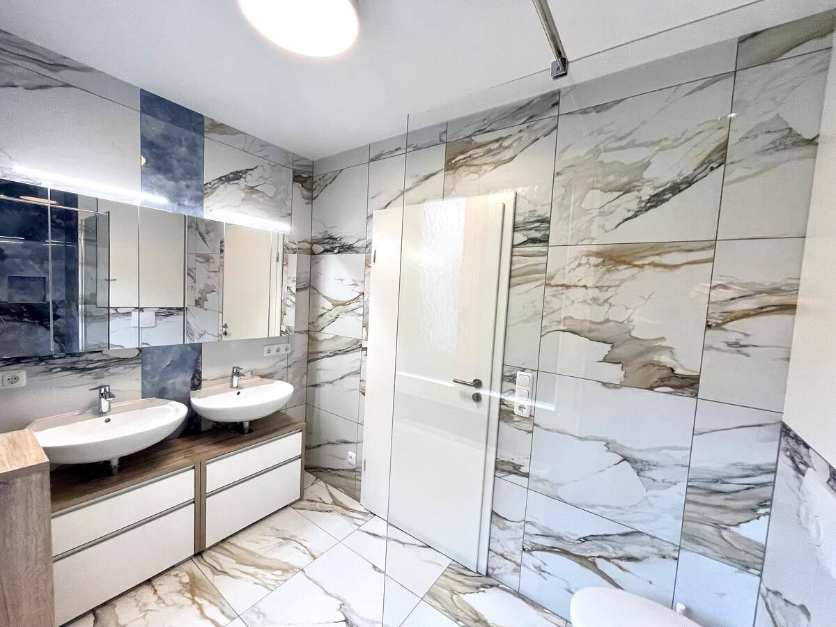 Modernes Badezimmer mit Doppelwaschbecken, großem Spiegelschrank und luxuriösen Marmorfliesen.