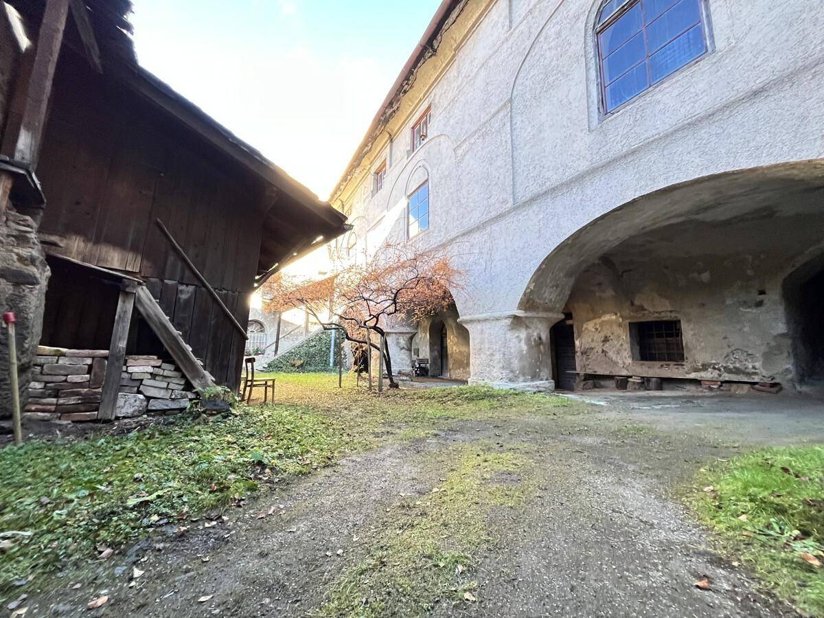 Historischer Innenhof mit altem Baumbestand, rustikalen Nebengebäuden und viel Grünfläche.