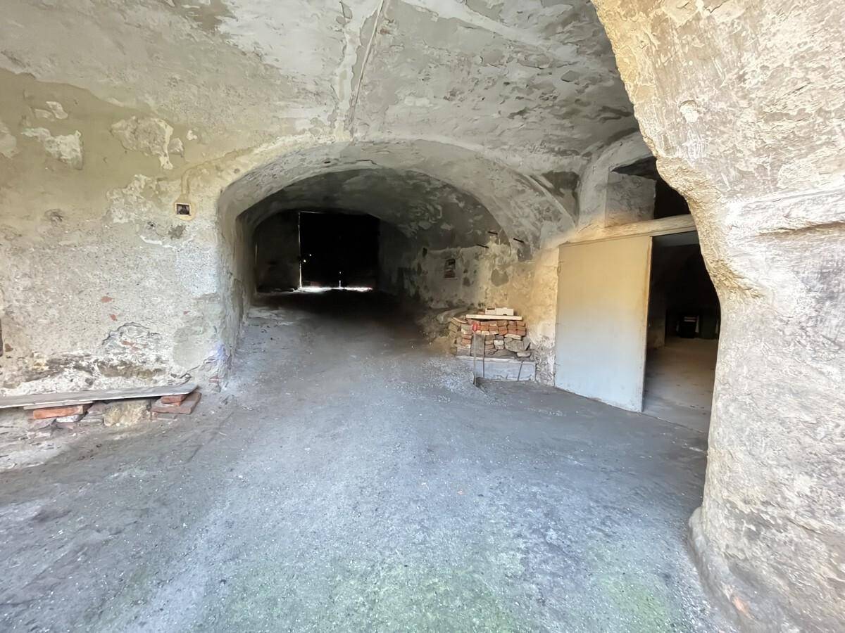 Gewölbter Eingangsbereich im Keller mit rustikalen Wänden und Betonboden, der in die Tiefe führt.