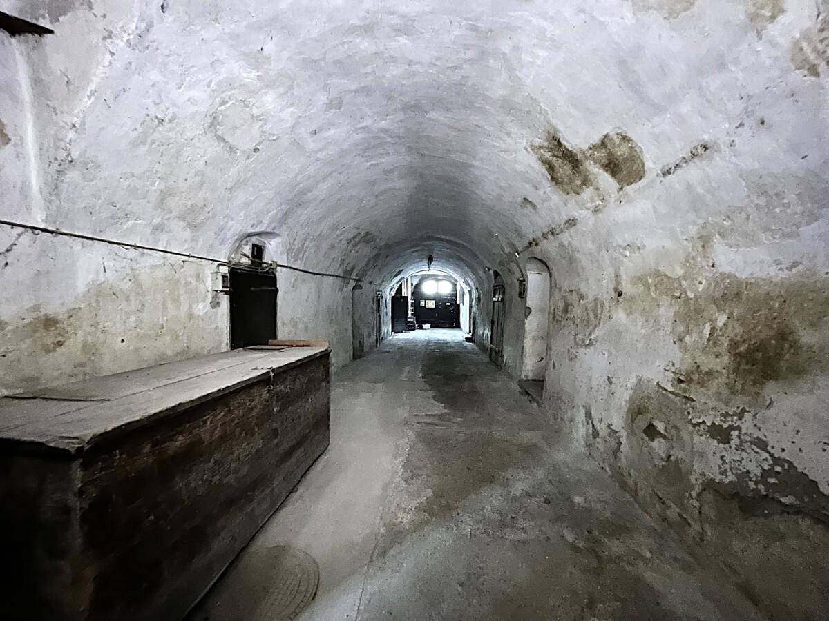 Langer, gewölbter Kellergang mit rustikalen Wänden und historischen Türen, der in die Tiefe führt.