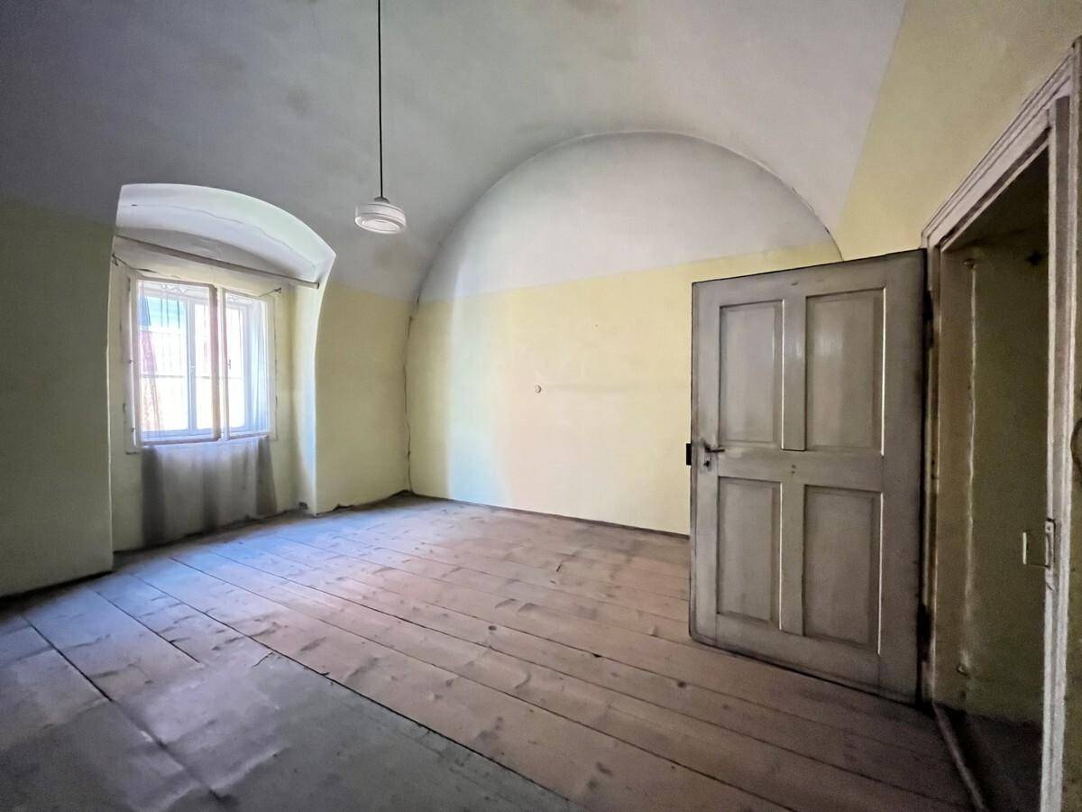 Leeres Zimmer mit Holzdielenboden, Gewölbedecke und einem Fenster, das Tageslicht hereinlässt.