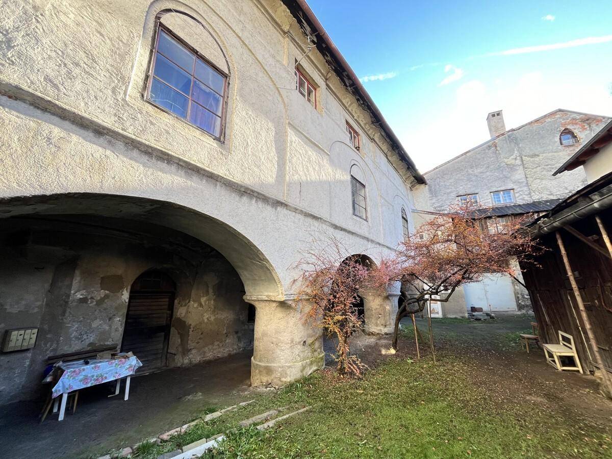Sonniger Innenhof mit alten Gebäudestrukturen, Bögen und einem kleinen Baum im Herbstlaub.
