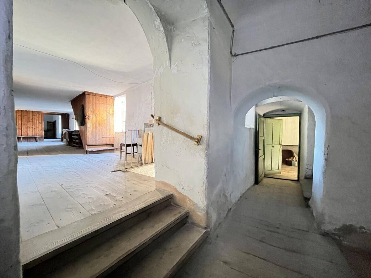 Geräumiger Flur mit Holzdielenboden, Treppe und gewölbten Durchgängen in einem alten Gebäude.