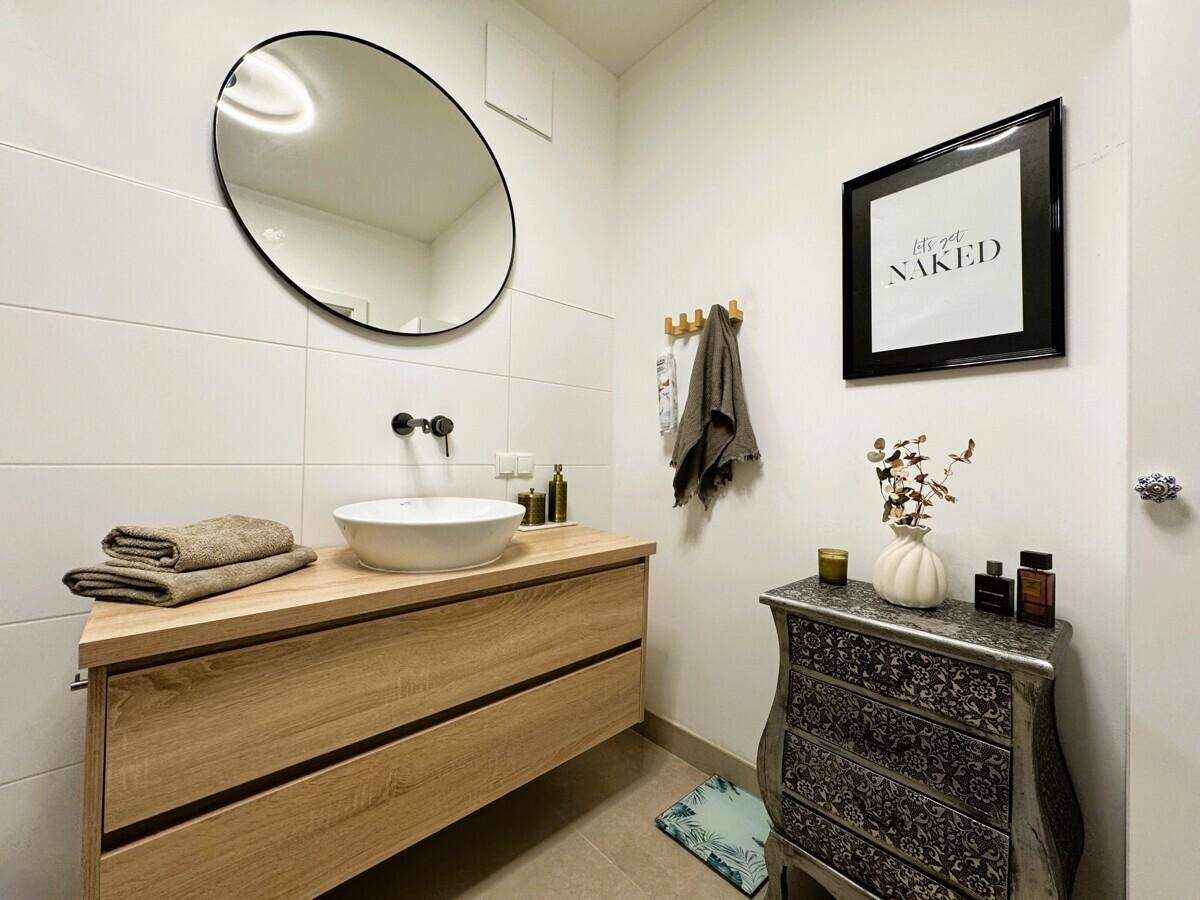 Modernes Badezimmer mit stilvollem Waschtisch, rundem Spiegel und weißer Wandfliesen.