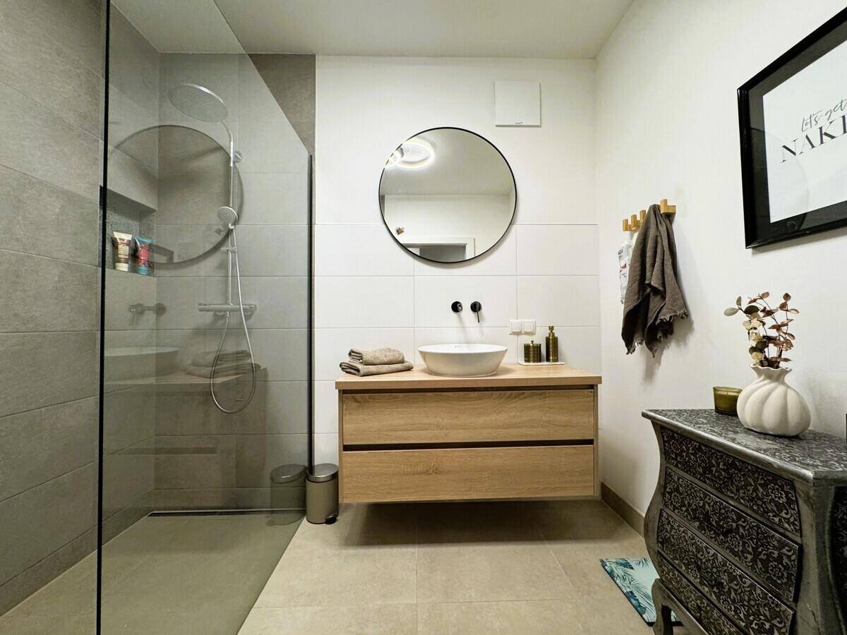 Modernes Badezimmer mit begehbarer Dusche, Holzwaschtisch und rundem Spiegel.