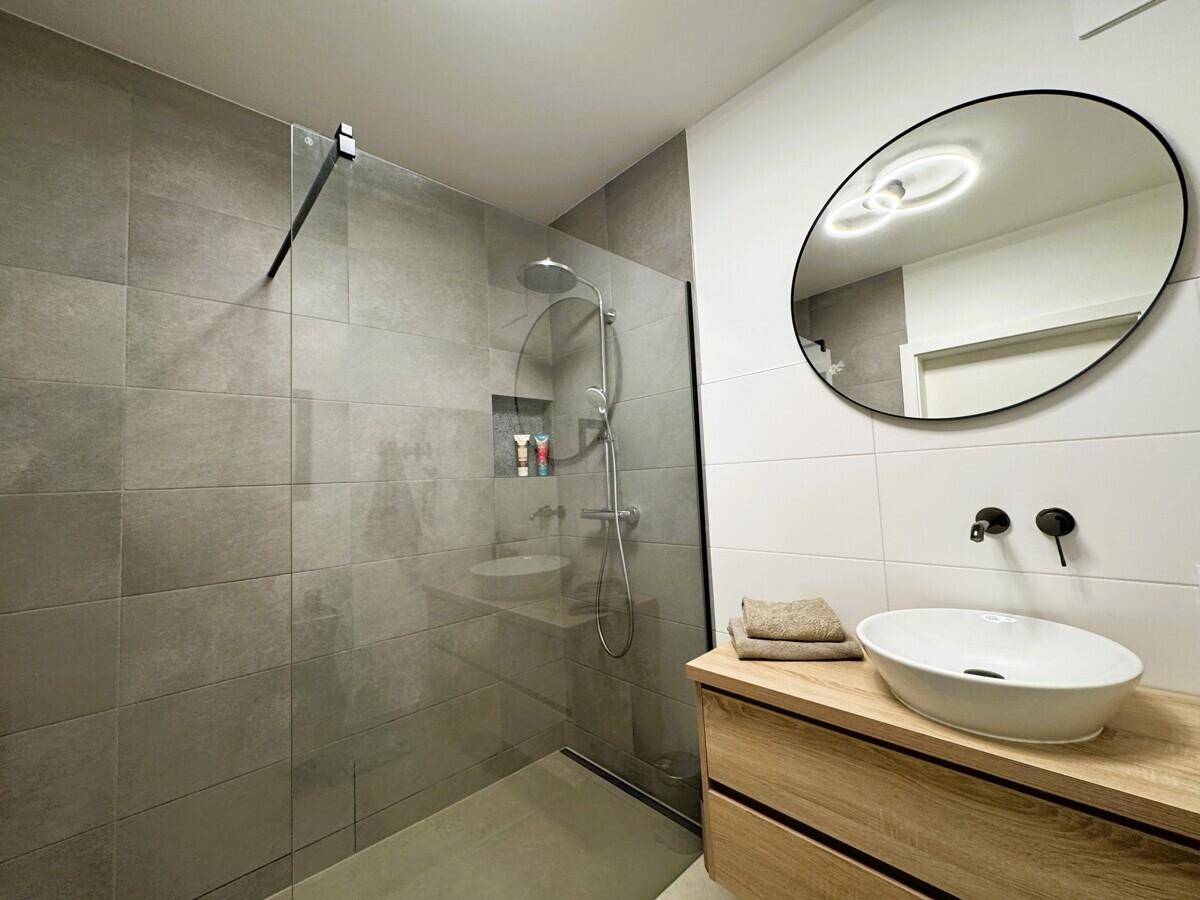 Elegantes Badezimmer mit begehbarer Dusche, modernem Waschtisch und großem Spiegel.