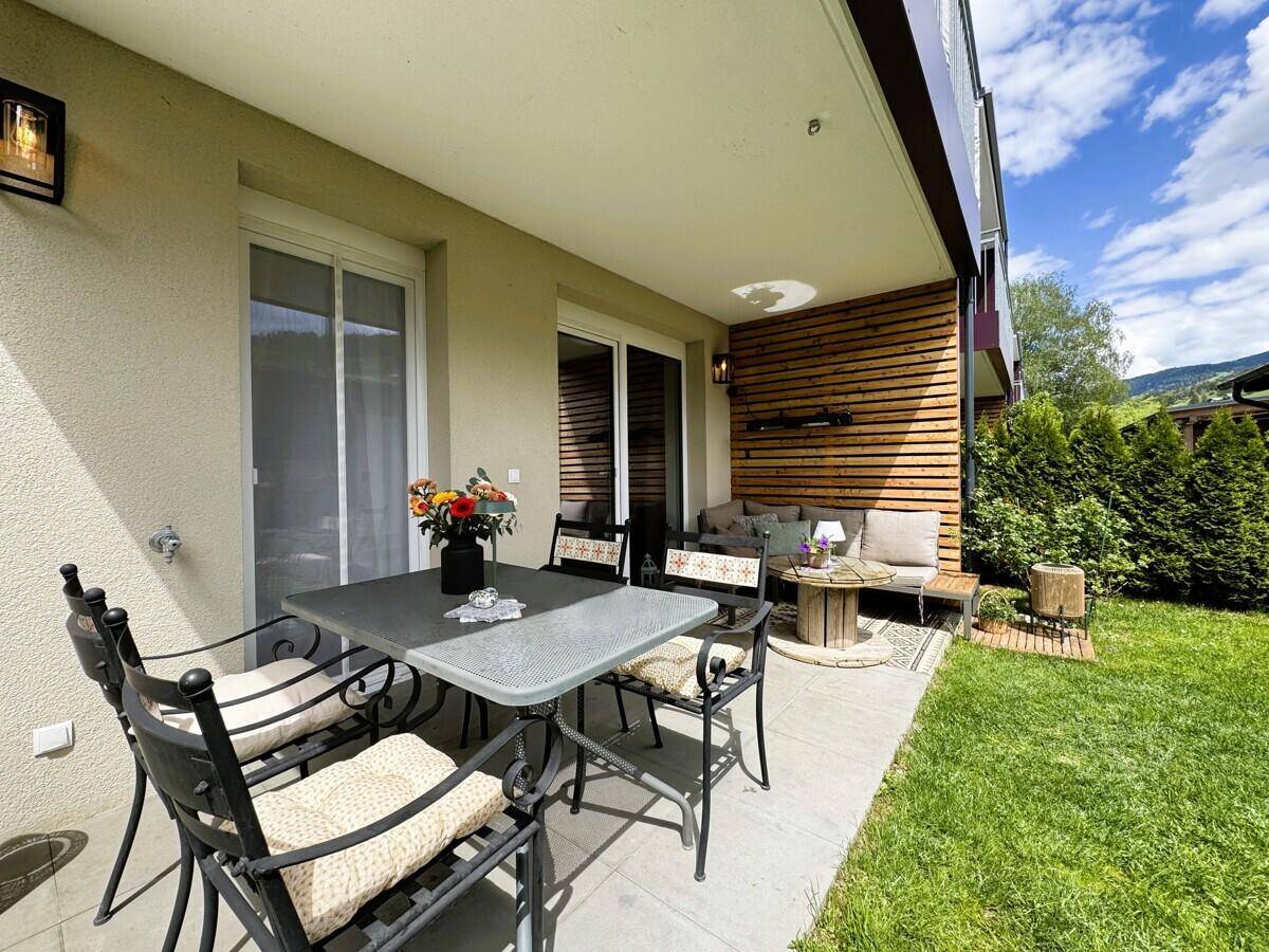 Sonnige Terrasse mit Esstisch und Lounge-Bereich, umgeben von einem gepflegten Garten.