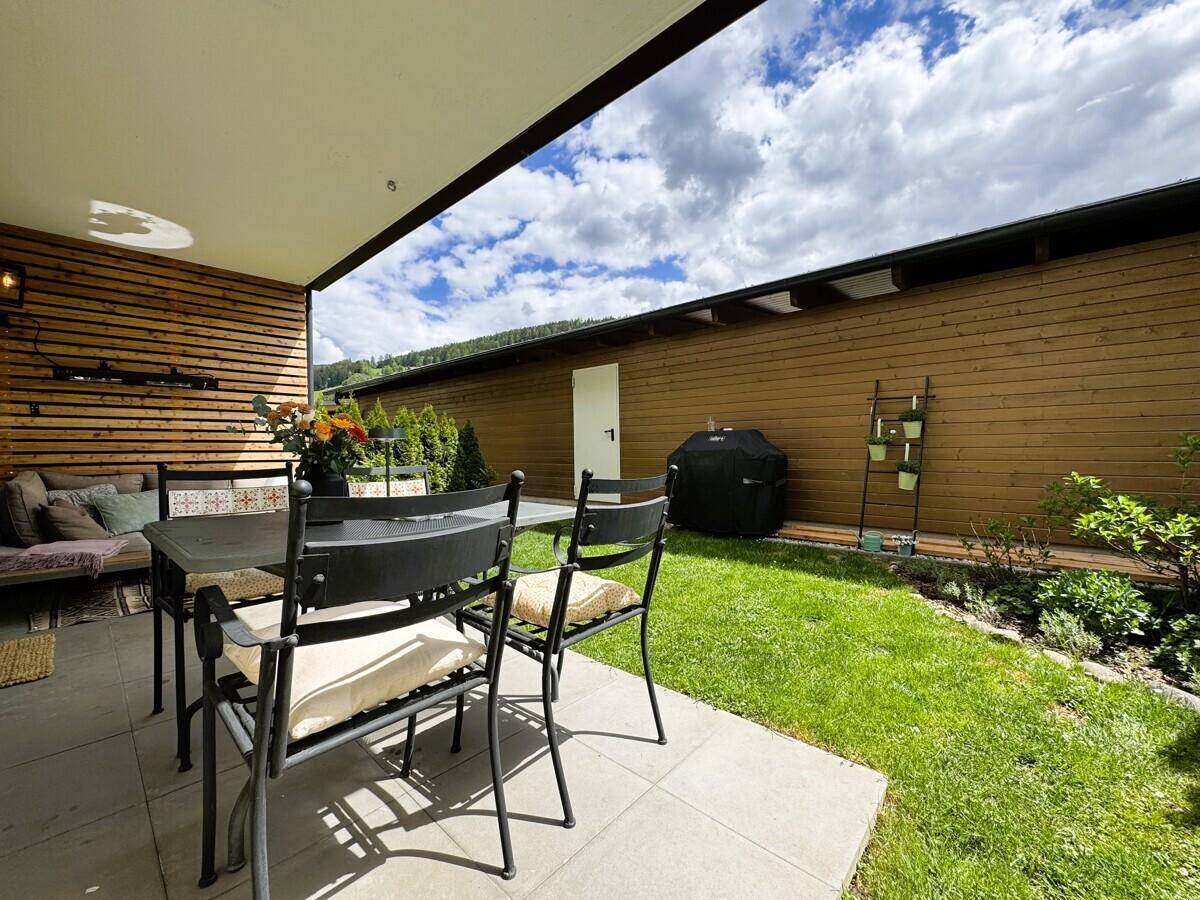 Terrasse mit Esstisch und Gartenblick, umgeben von einer Holzwand und Hecken.