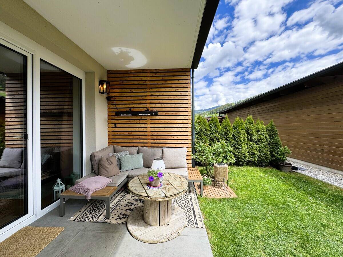 Gemütlicher Lounge-Bereich auf der Terrasse mit Holzwand und Blick ins Grüne.
