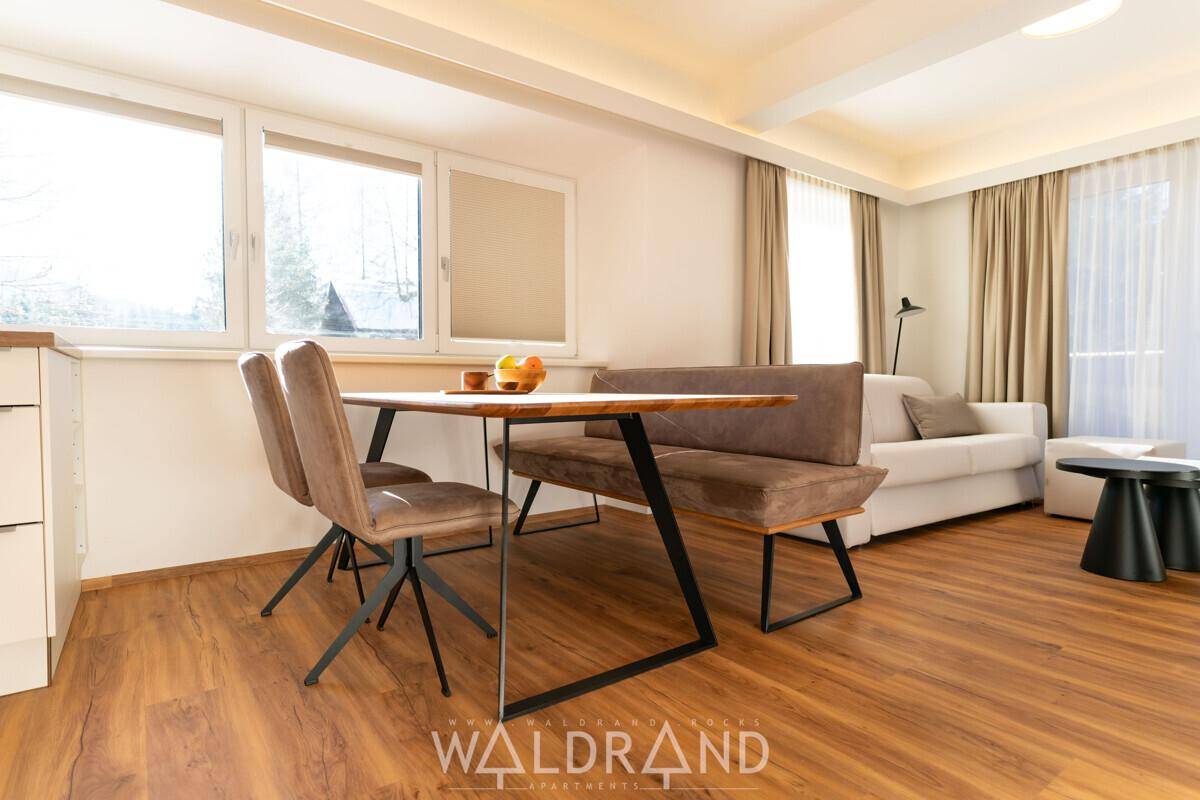 Gemütlicher Wohn-Essbereich mit Holzboden, Esstisch und Sofa, hell durch große Fenster.