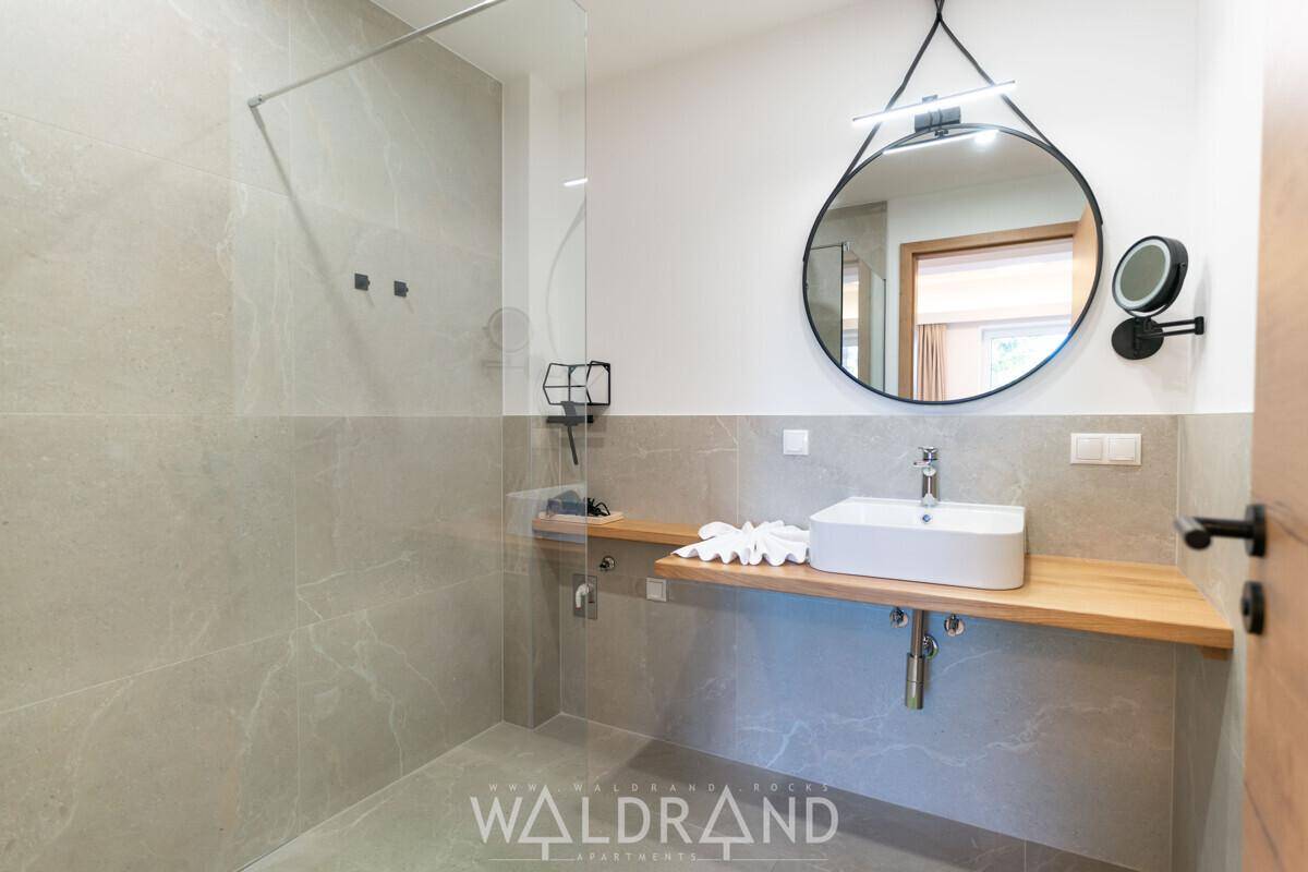 Modernes Badezimmer mit begehbarer Dusche, Einzelwaschbecken und großem runden Spiegel.