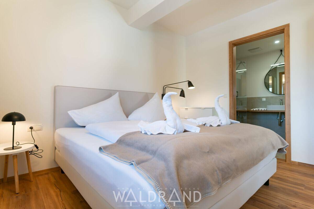 Schlafzimmer mit Doppelbett und Holzboden, direkter Zugang zu einem modernen Badezimmer.