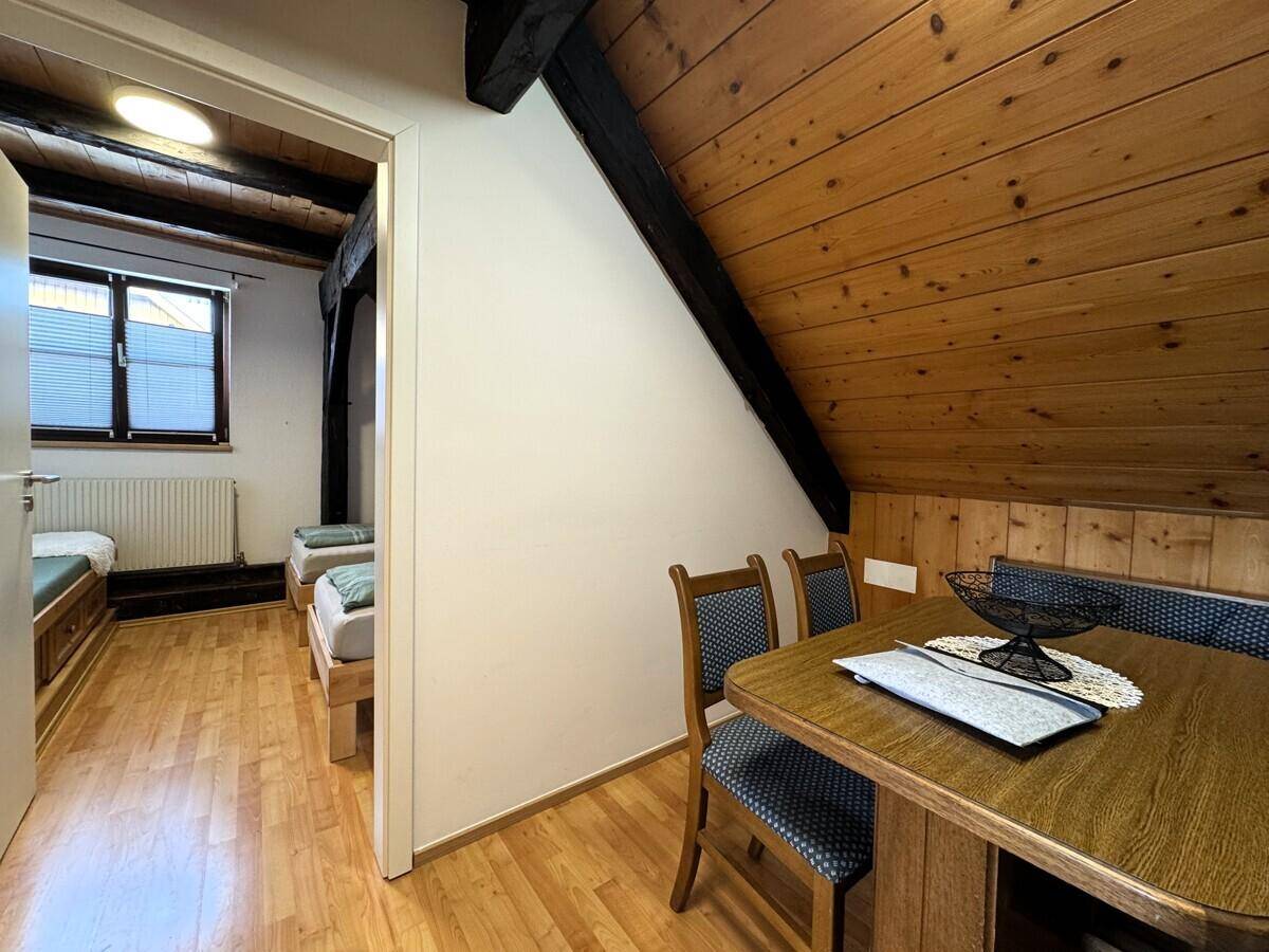 Essbereich mit Blick in ein Schlafzimmer, beide mit Holzdachschräge und Holzboden.