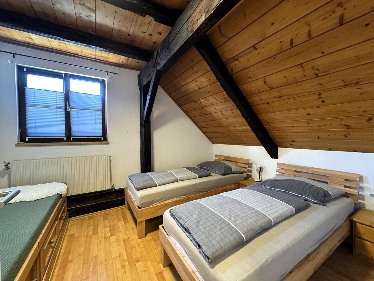 Schlafzimmer im Dachgeschoss mit zwei Einzelbetten, Holzboden und Dachschräge.