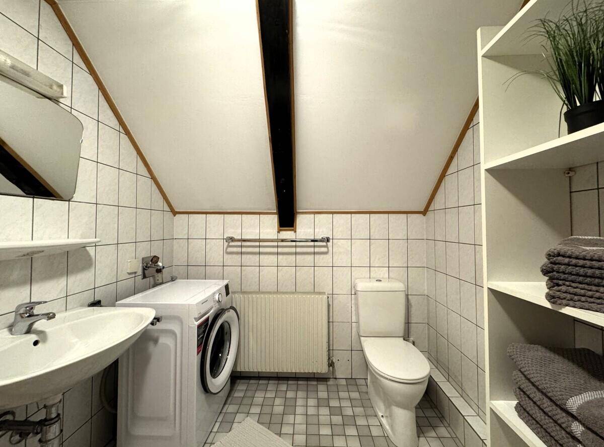 Badezimmer mit Waschmaschine, WC, Waschbecken und gefliesten Wänden im Dachgeschoss.