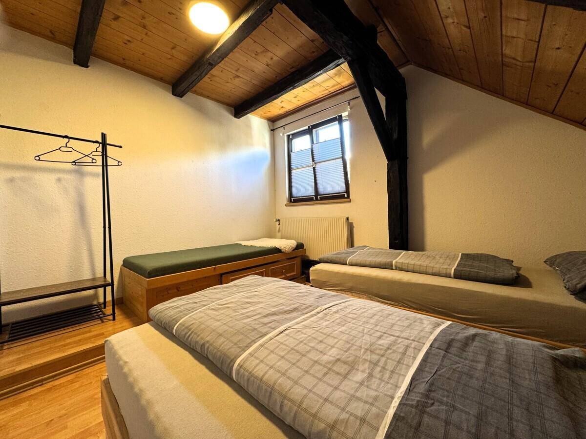 Helles Schlafzimmer mit Holzdecken, zwei Betten und einem Kleiderständer.