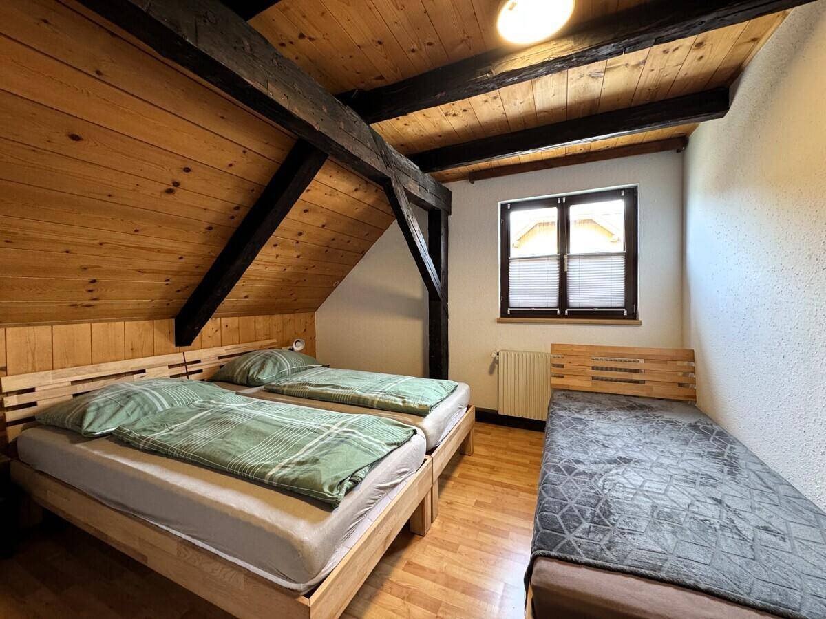 Geräumiges Schlafzimmer mit Holzdecken, drei Betten und Fenster, ideal für Familien.