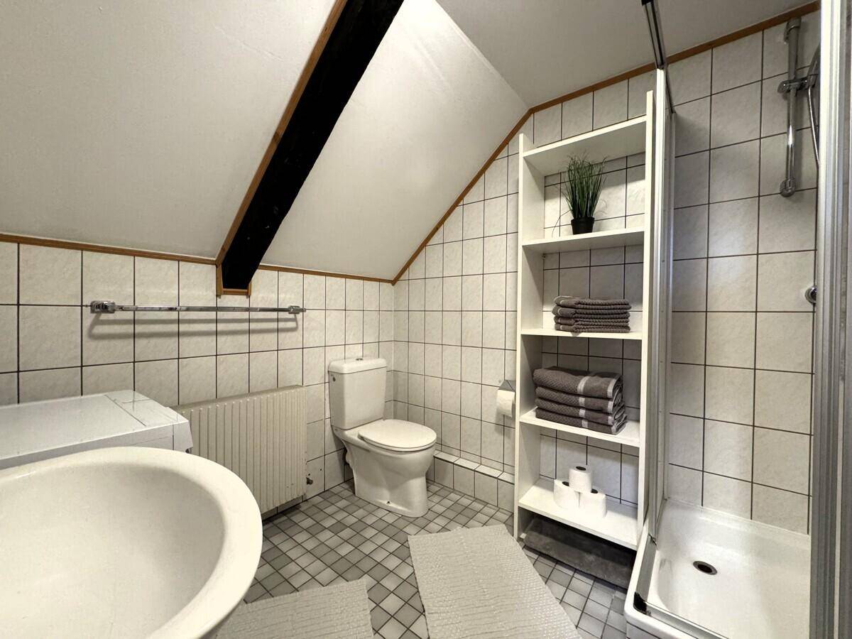 Gefliestes Badezimmer mit Dusche, WC, Regal und Dachschräge, funktional eingerichtet.
