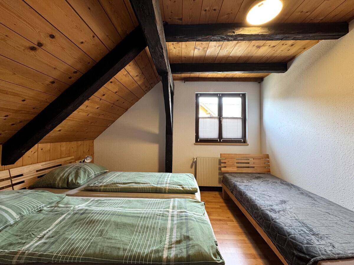 Schlafzimmer mit drei Betten, Holzboden und Holzdachschräge, hell beleuchtet.