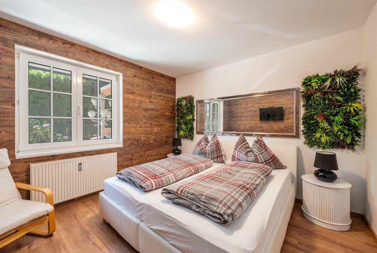 Helles Schlafzimmer mit Holzwand, Doppelbett und großem Spiegel über dem Kopfteil.