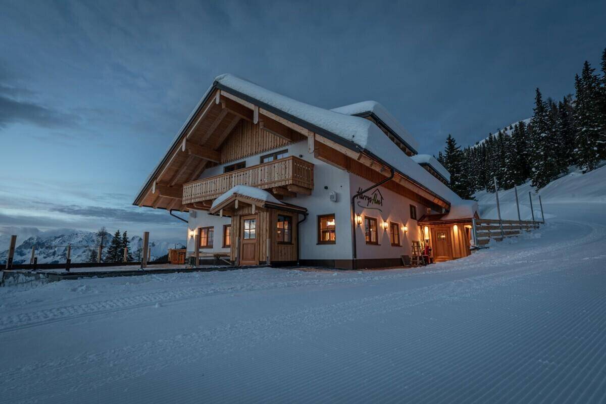 Alpines Chalet in der Dämmerung mit beleuchteten Fenstern und verschneiter Umgebung.