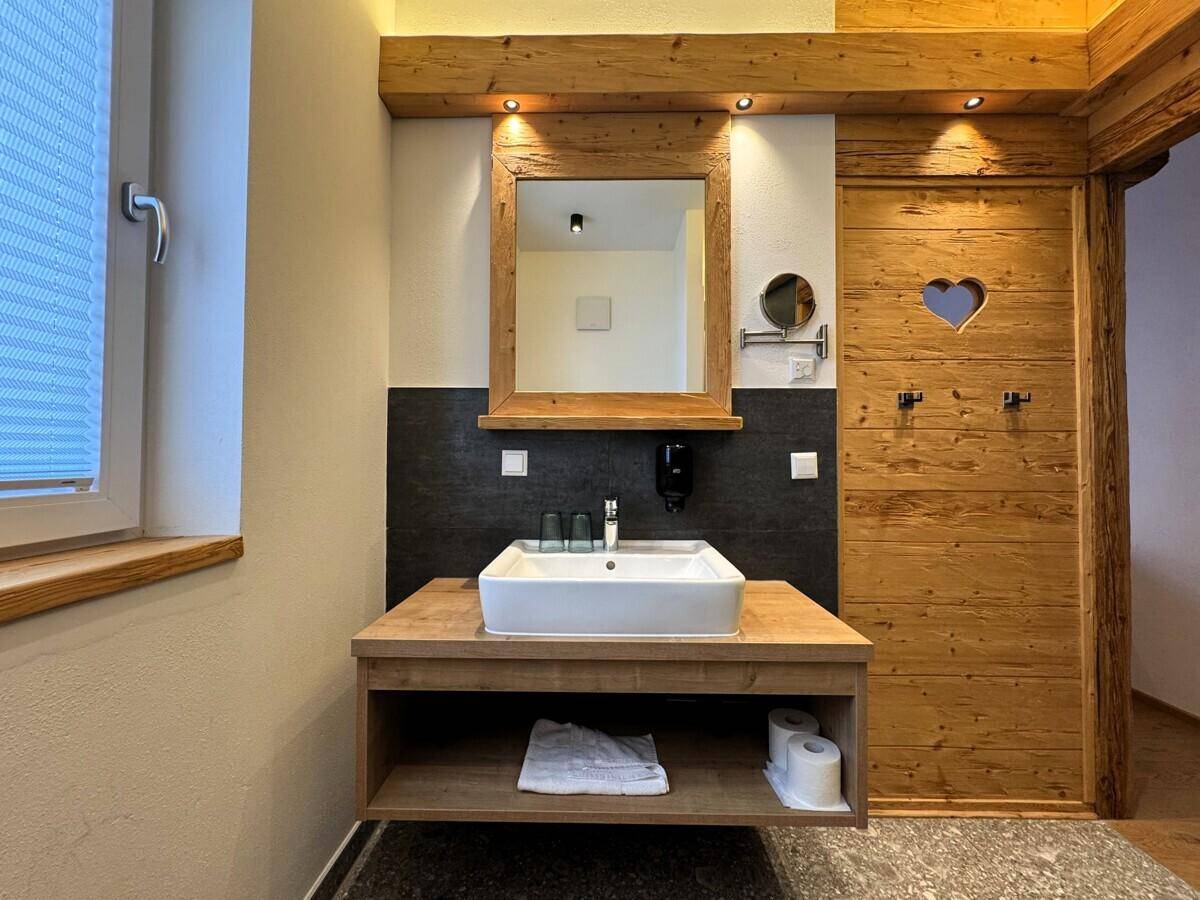 Modernes Badezimmer mit Holzwaschtisch, großem Spiegel und dunklen Fliesenakzenten.