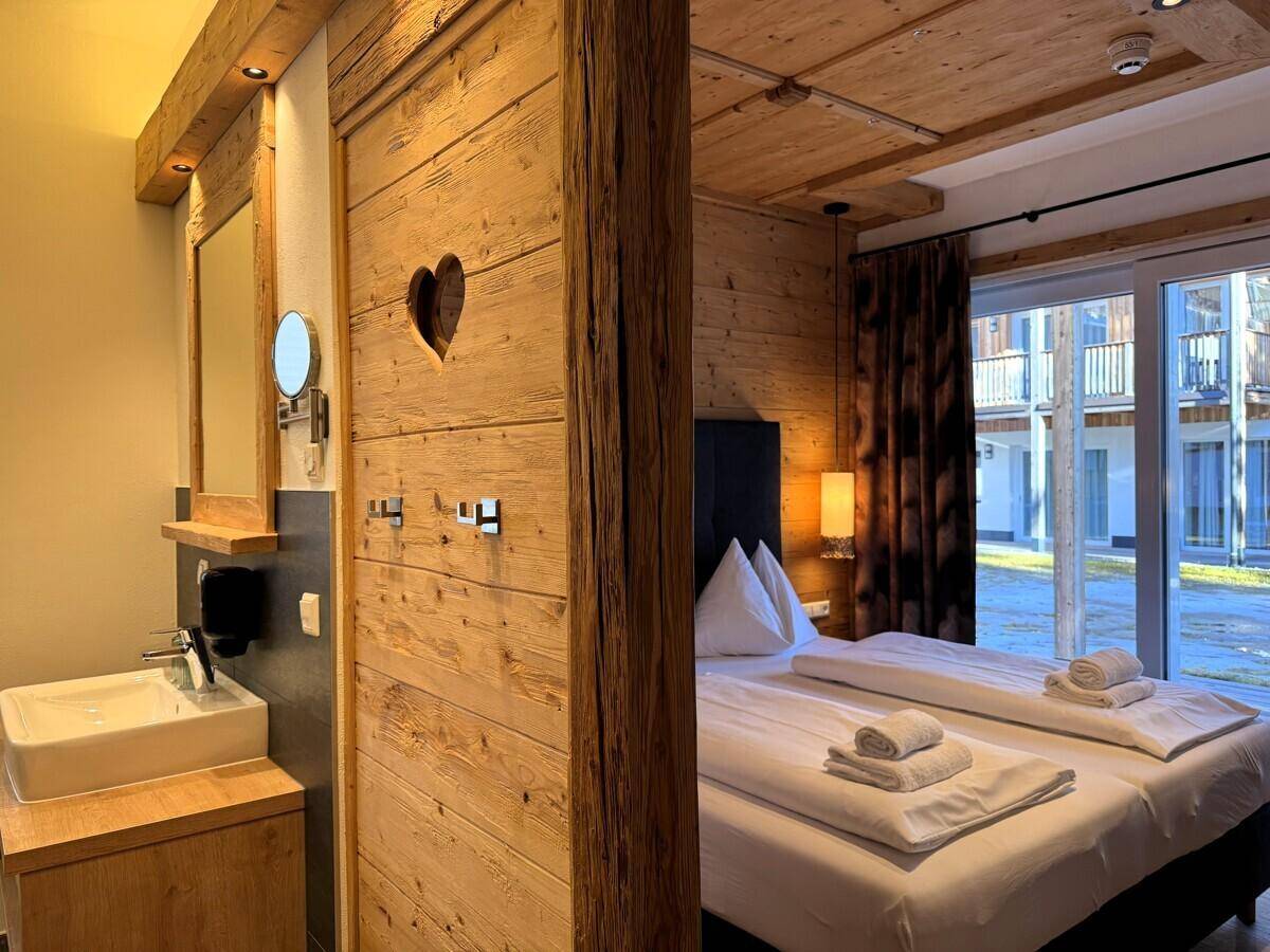 Schlafzimmer mit integriertem Waschbeckenbereich, Holzwänden und Zugang zu einer Terrasse.