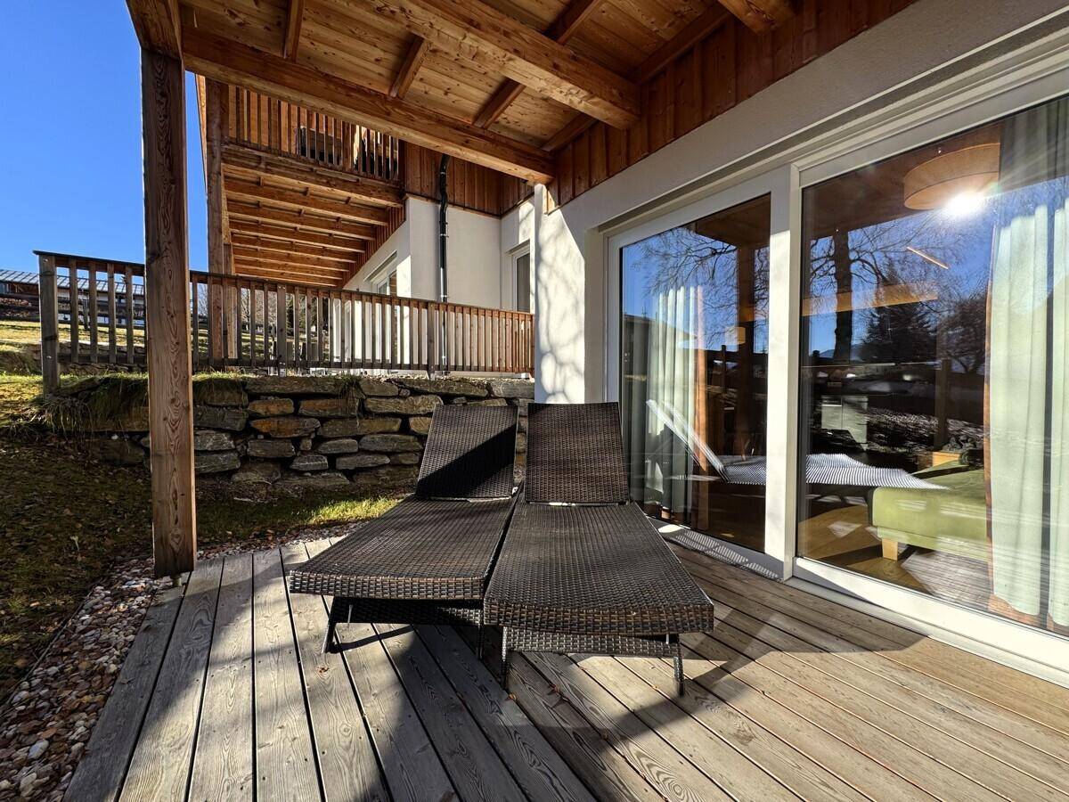 Holzterrasse mit bequemen Sonnenliegen und Blick auf die moderne Gebäudefassade.