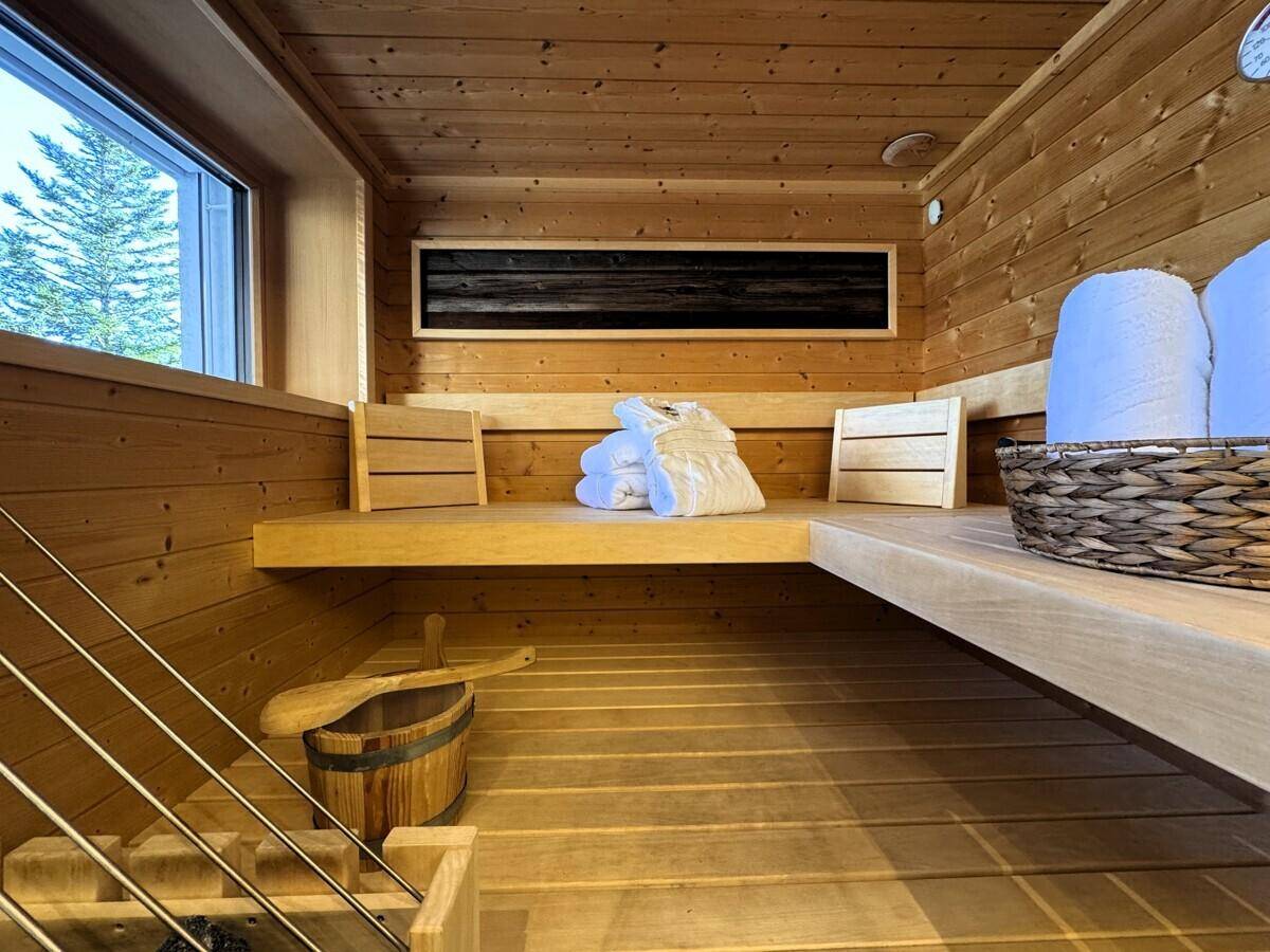 Innenansicht der Sauna mit Holzbänken, Fenster und traditionellem Aufgusseimer.