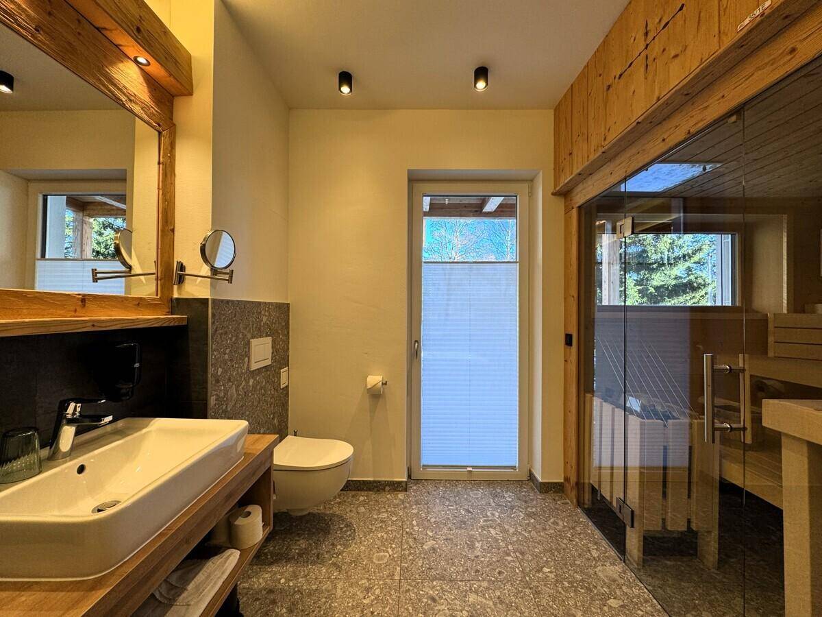 Modernes Badezimmer mit Einzelwaschbecken, Toilette und direktem Zugang zur Sauna.