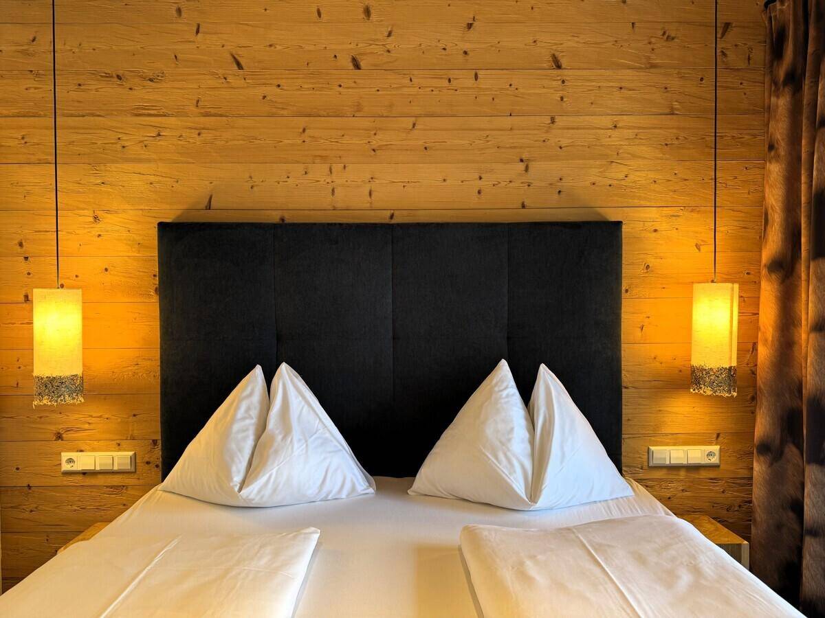 Gemütliches Schlafzimmer mit Doppelbett, Holzwänden und warmen Nachttischlampen.