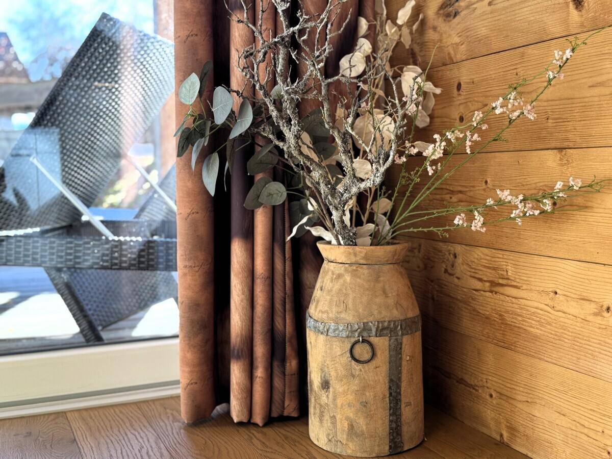 Dekorative Vase mit getrockneten Ästen neben einem Fenster mit braunen Vorhängen.