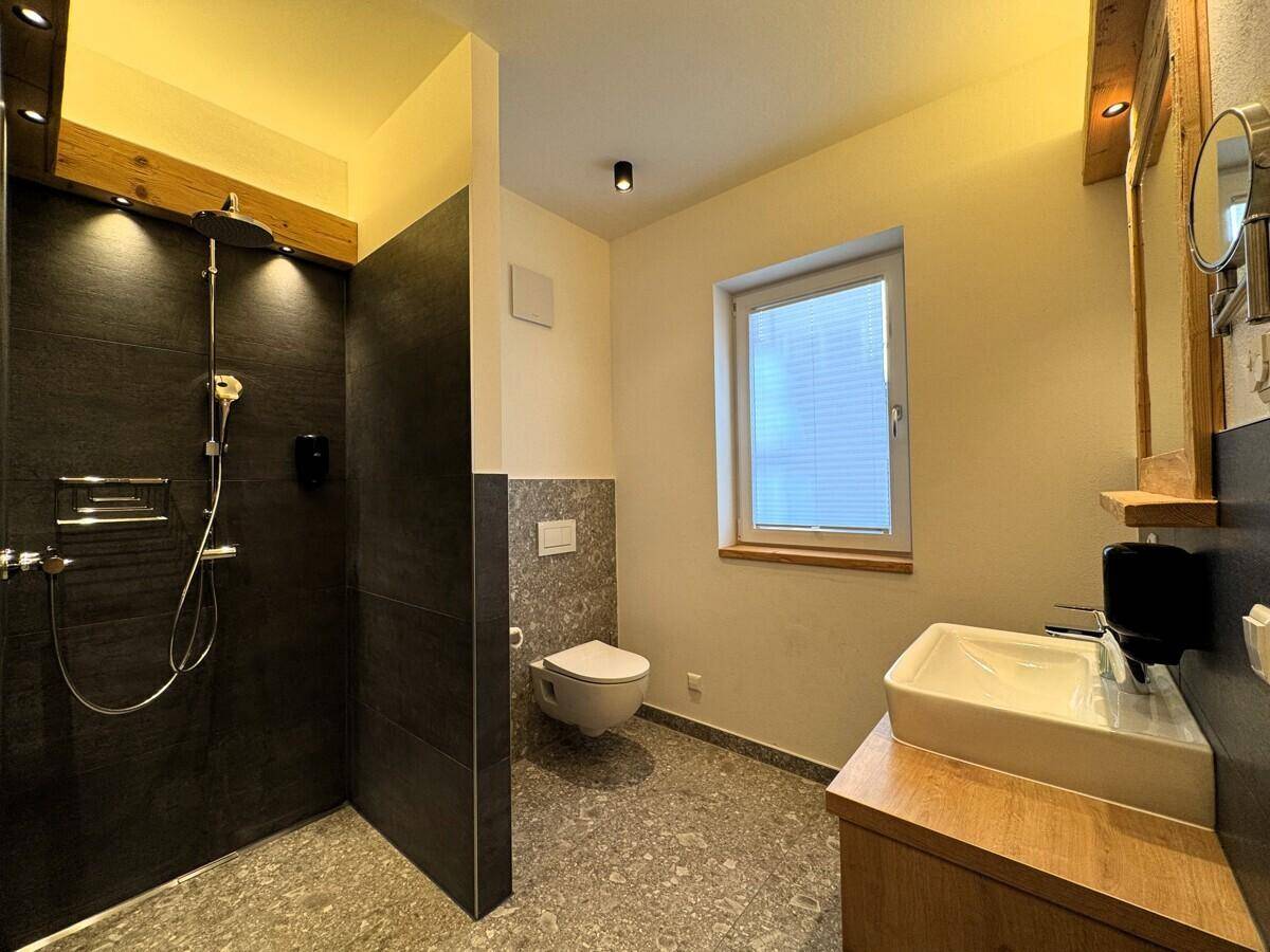 Helles Badezimmer mit ebenerdiger Dusche, wandhängendem WC und Fenster für Tageslicht.