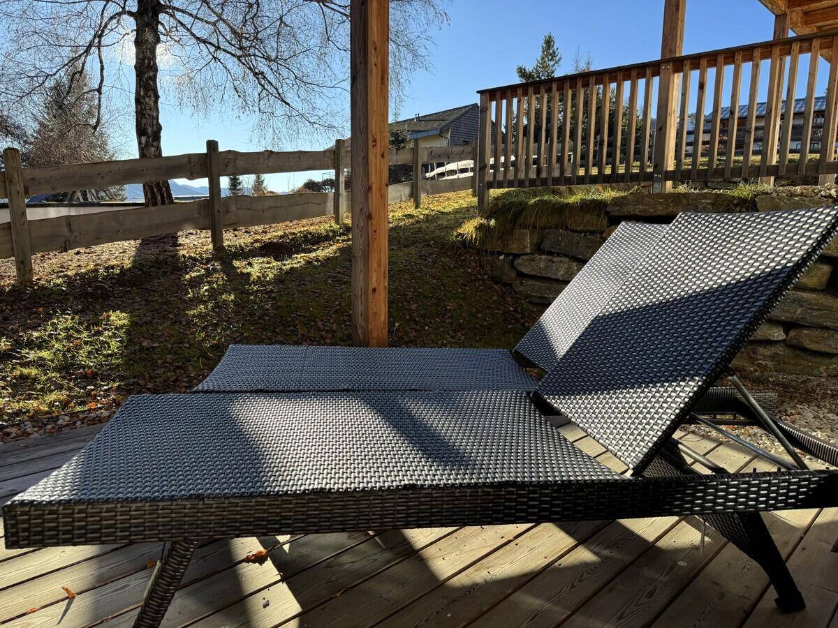 Nahaufnahme einer modernen Sonnenliege auf einer Holzterrasse unter blauem Himmel.