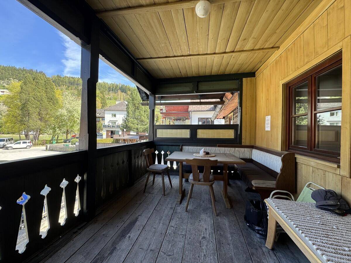 Großer überdachter Holzbalkon mit Esstisch und weitem Blick ins Grüne.